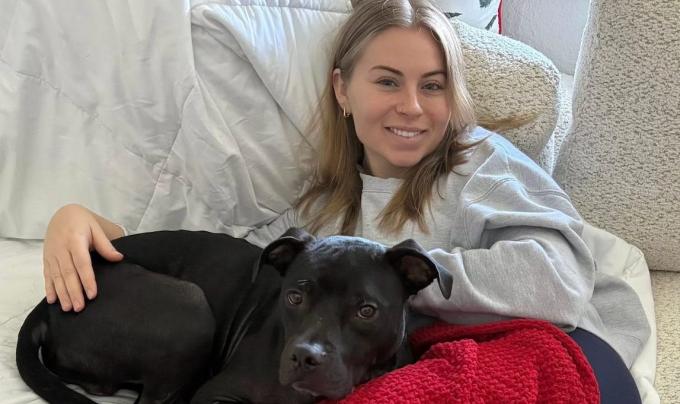 Eli the dog snuggling with Makenna Carew on a bed
